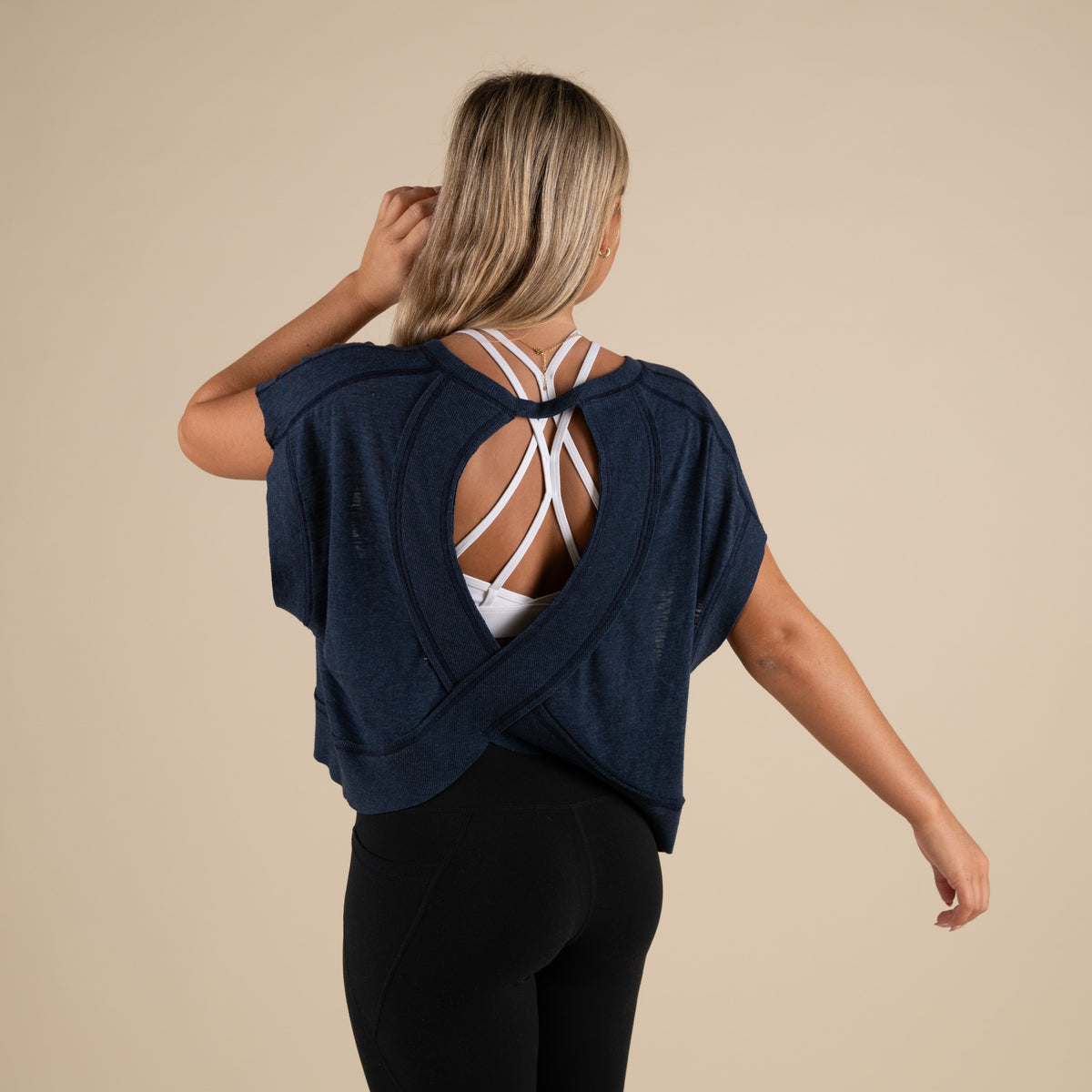 Woman wearing a navy blue activewear top with a cutout back and black leggings.