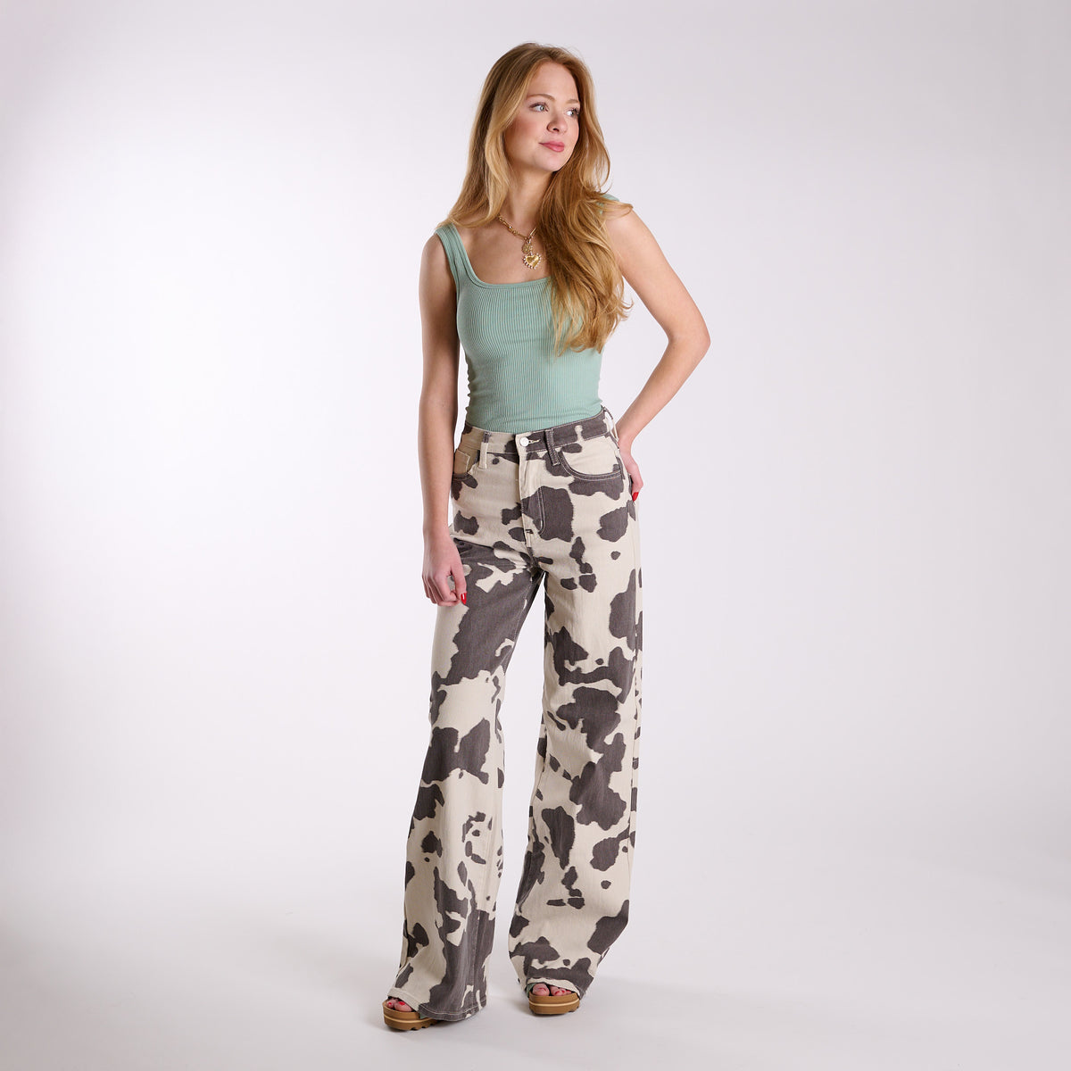 Women’s cow print wide-leg jeans styled on model with full-body angled view, high-rise fit, wide legs, and cream and brown cow print pattern.