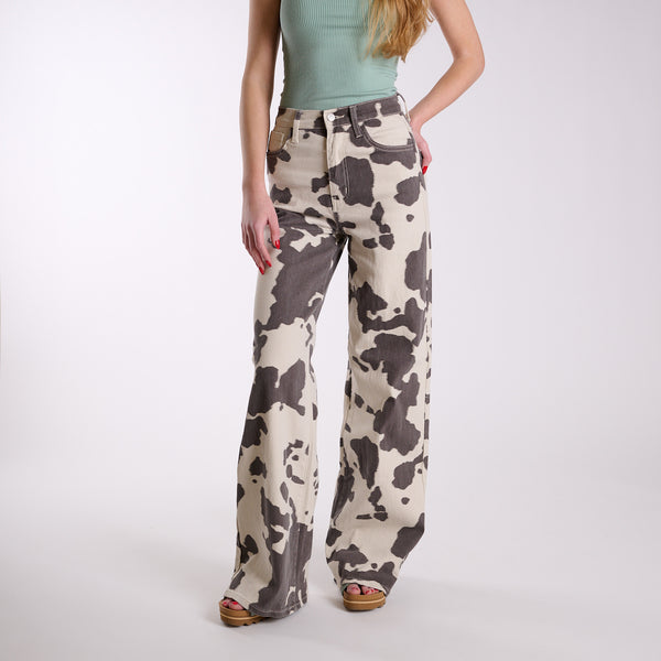 Women’s cow print wide-leg jeans with full front view, high-rise waist, button and zip closure, and wide legs in cream and brown cow print.