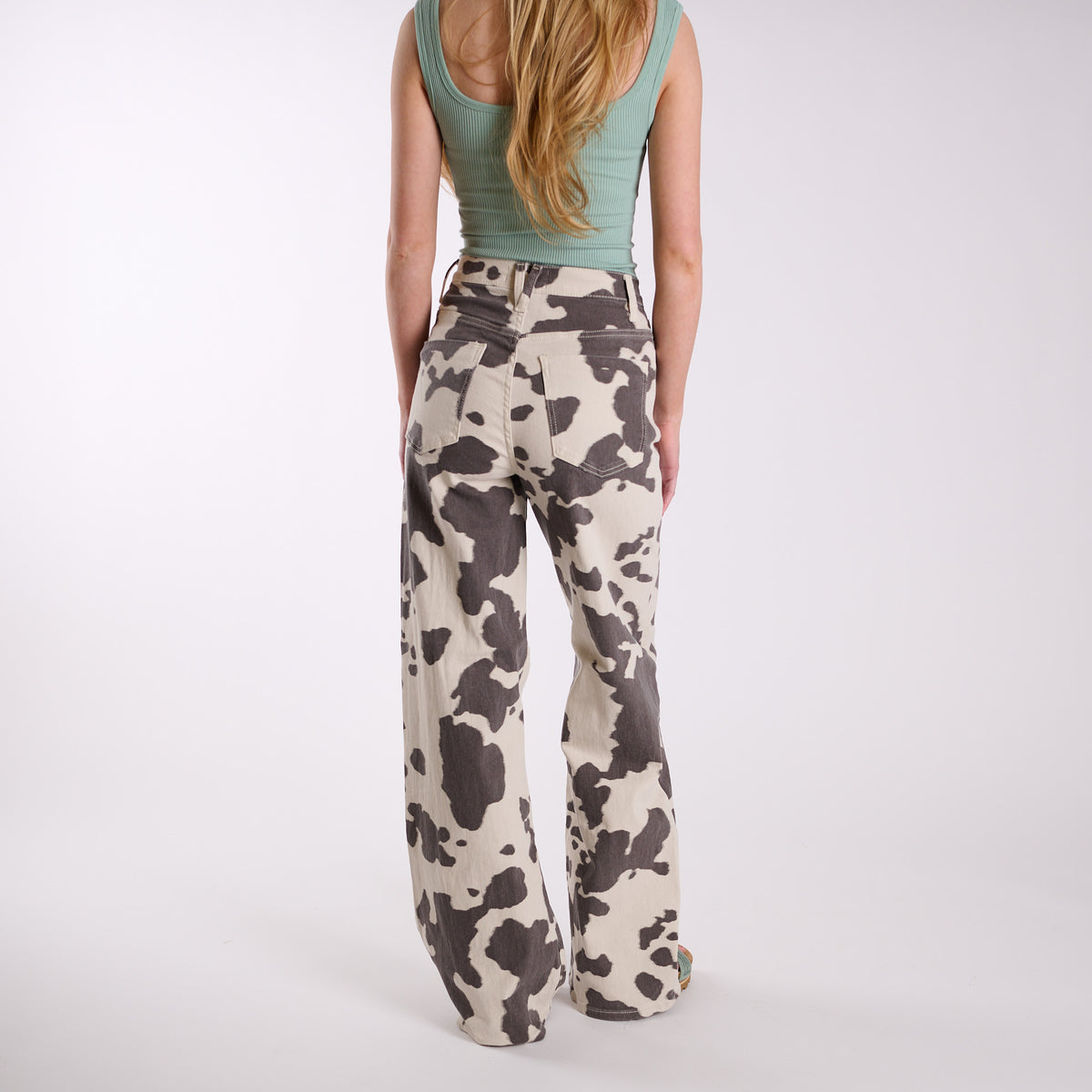 Women’s cow print wide-leg jeans with full back view, high-rise fit, back pockets, and wide-leg silhouette in cream and brown cow print.