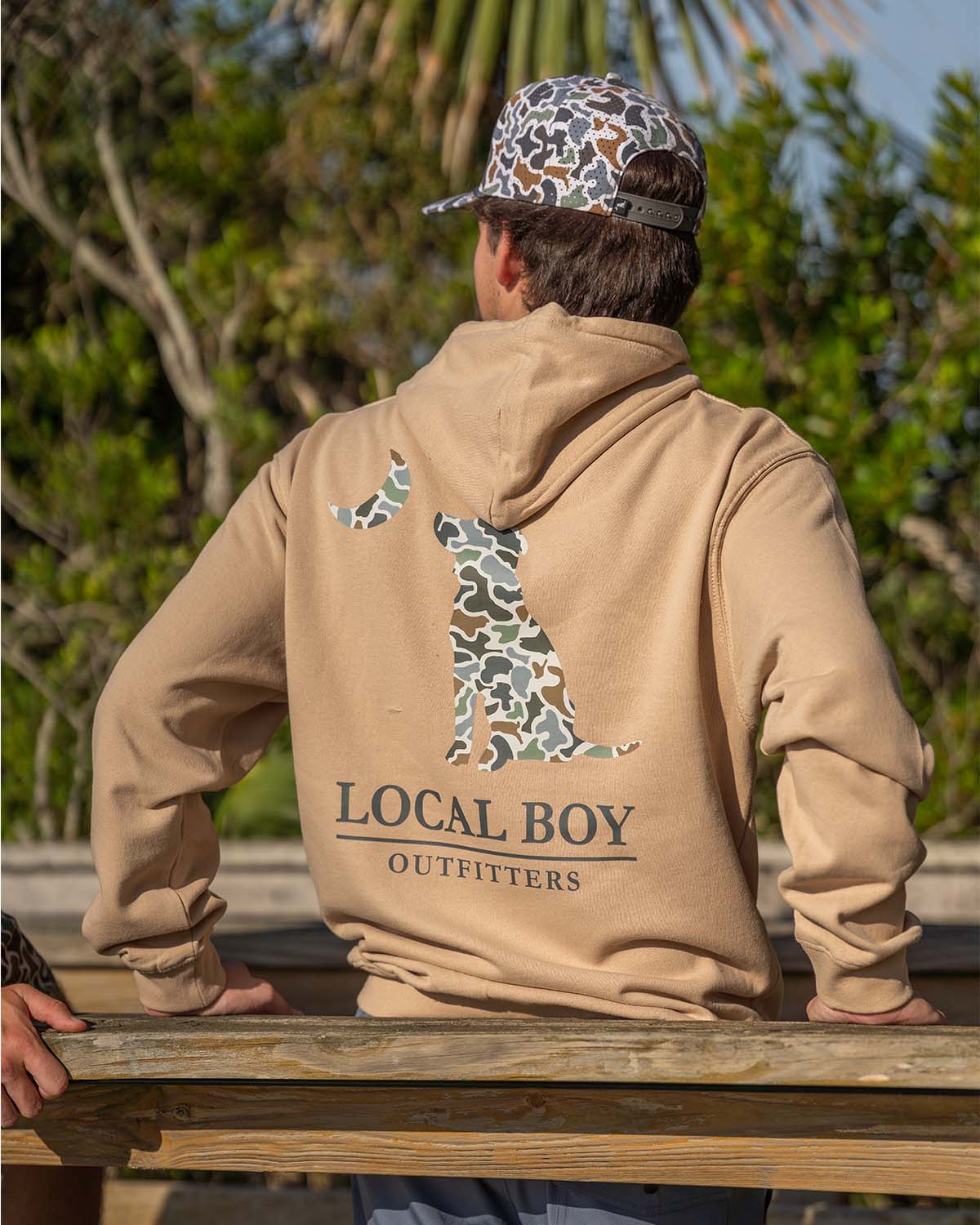 A man standing with his back turned to the camera wearing a local boy sweatshirt.