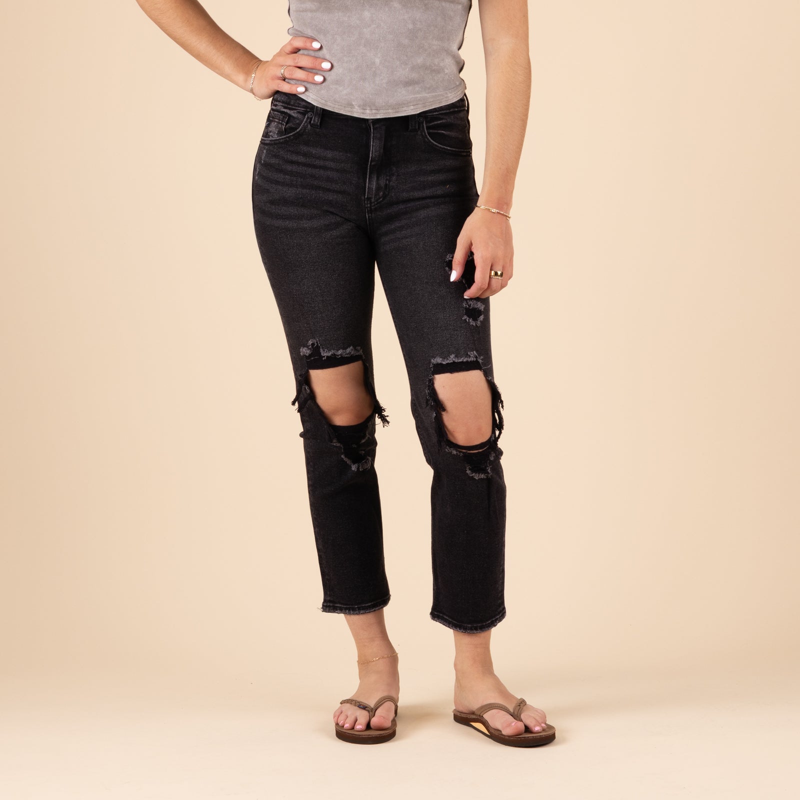 Front view of a woman wearing black straight-leg jeans with a mid to high-rise fit and distressed detailing at both knees. The jeans have a clean hem, minimal fading, and a structured silhouette. Styled with a casual top and shoes, against a neutral background.