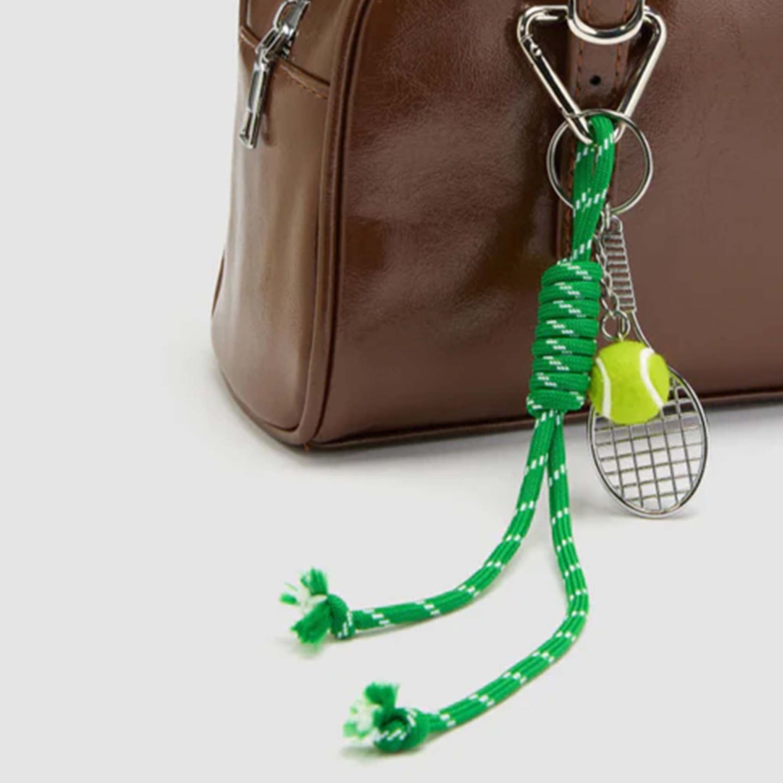 Serve up some serious style with this playful tennis-themed bag charm! Featuring sporty-chic details like a mini racket, green tennis ball, and green cord detail, it’s the perfect accessory for tennis lovers and fashionistas alike. This chain clips to any bag using a carabiner style keychain.