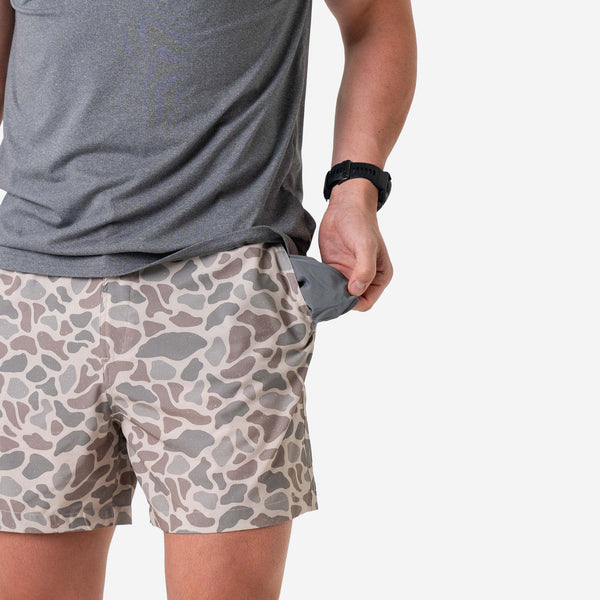 Man wearing Burlebo Everyday Shorts in Classic Deer Camo and a grey t-shirt in front of a white background