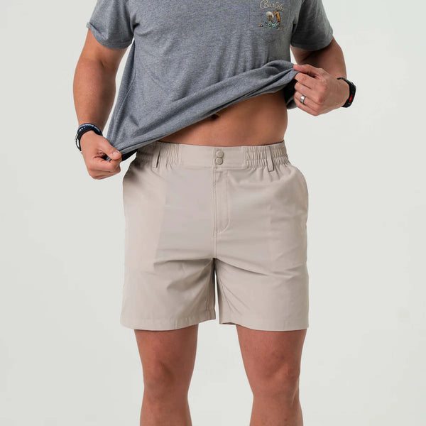 Man wearing Burlebo light khaki shorts, lifting shirt to show elastic waistband and button closure.