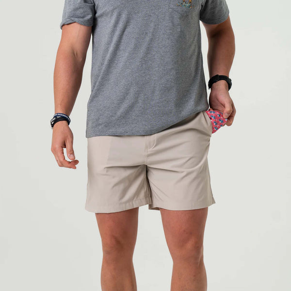 Man wearing Burlebo light khaki hybrid shorts, pulling out American flag print lining from side pocket.