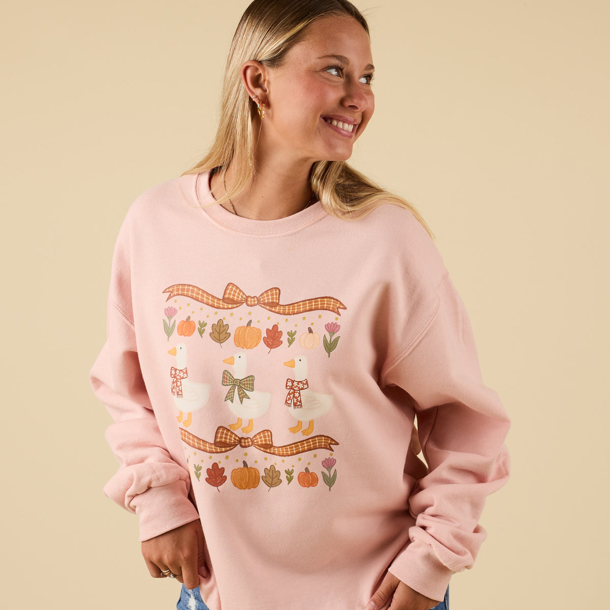 Side angle of model wearing pink sweatshirt with festive autumn geese and bow print.