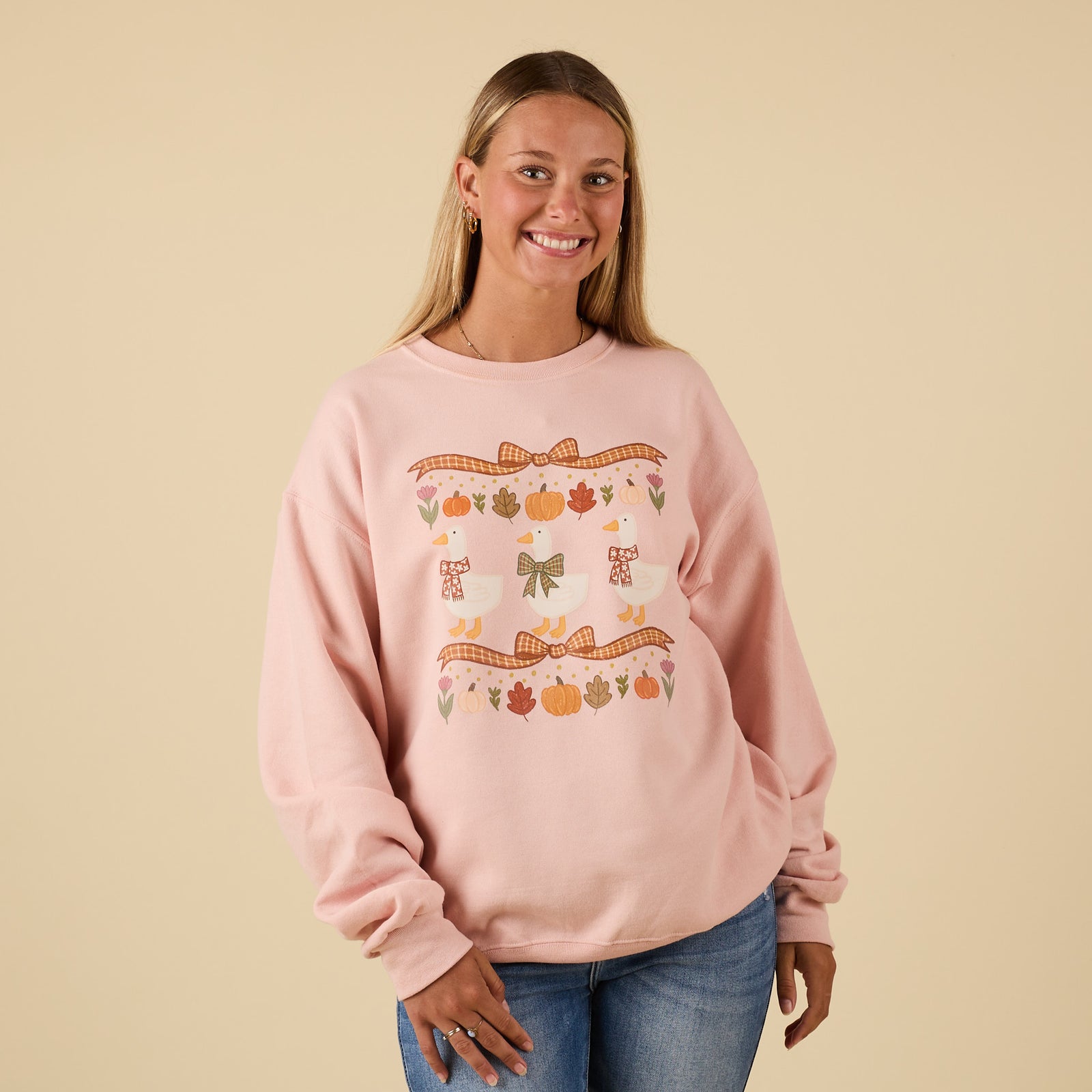 Front view of pink crewneck sweatshirt with fall-themed design of geese, bows, pumpkins, and leaves.