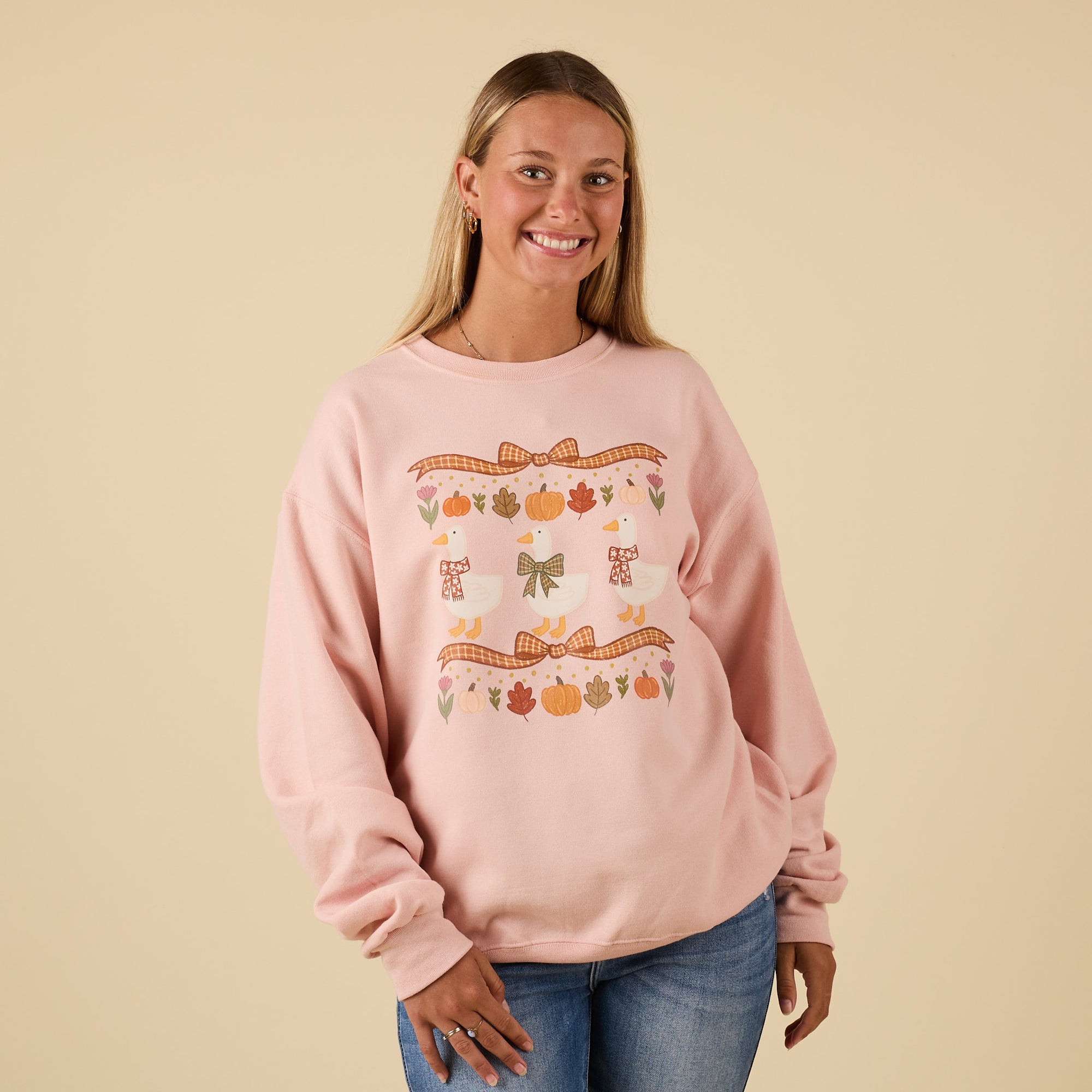 Front view of pink crewneck sweatshirt with fall-themed design of geese, bows, pumpkins, and leaves.