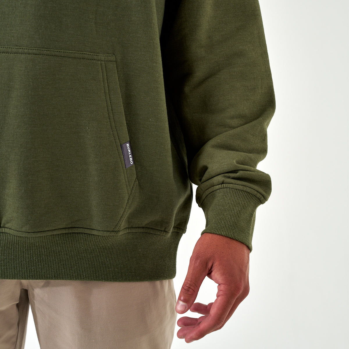Detail view of front kangaroo pocket with Burlebo logo tag on olive green hoodie.