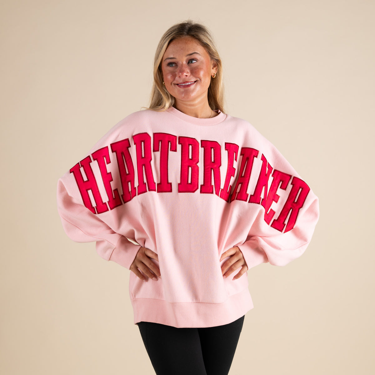 Person wearing a pink sweatshirt with 'HEARTBREAKER' in red text on a beige background