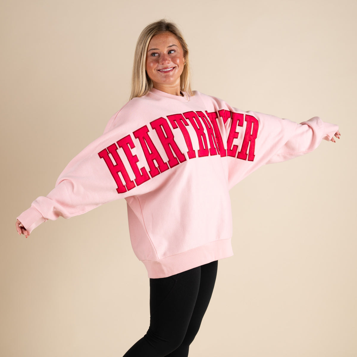 Person wearing a pink sweatshirt with 'HEARTBREAKER' in red letters on a beige background