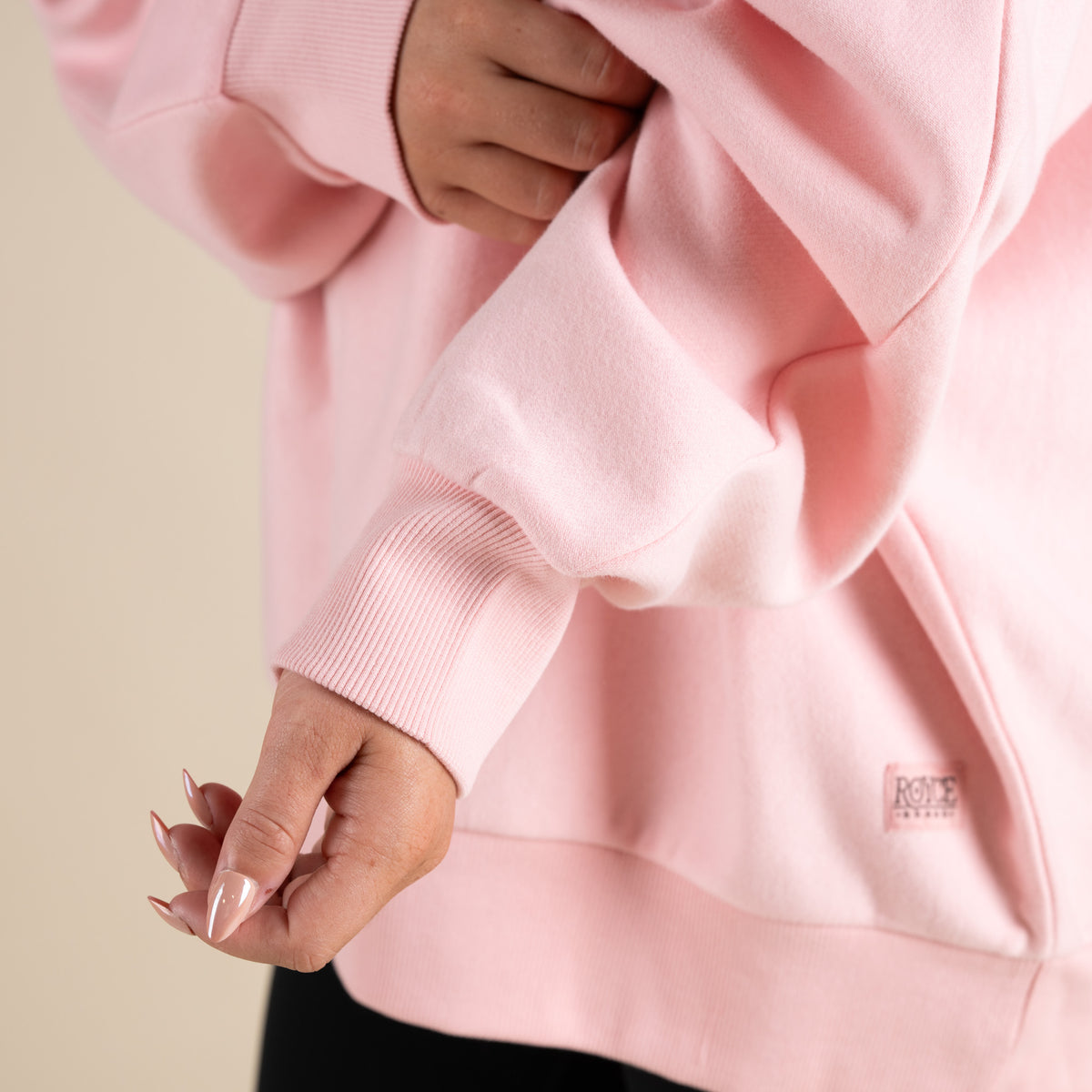 Close-up of a pink sweatshirt with a brand logo on a beige background