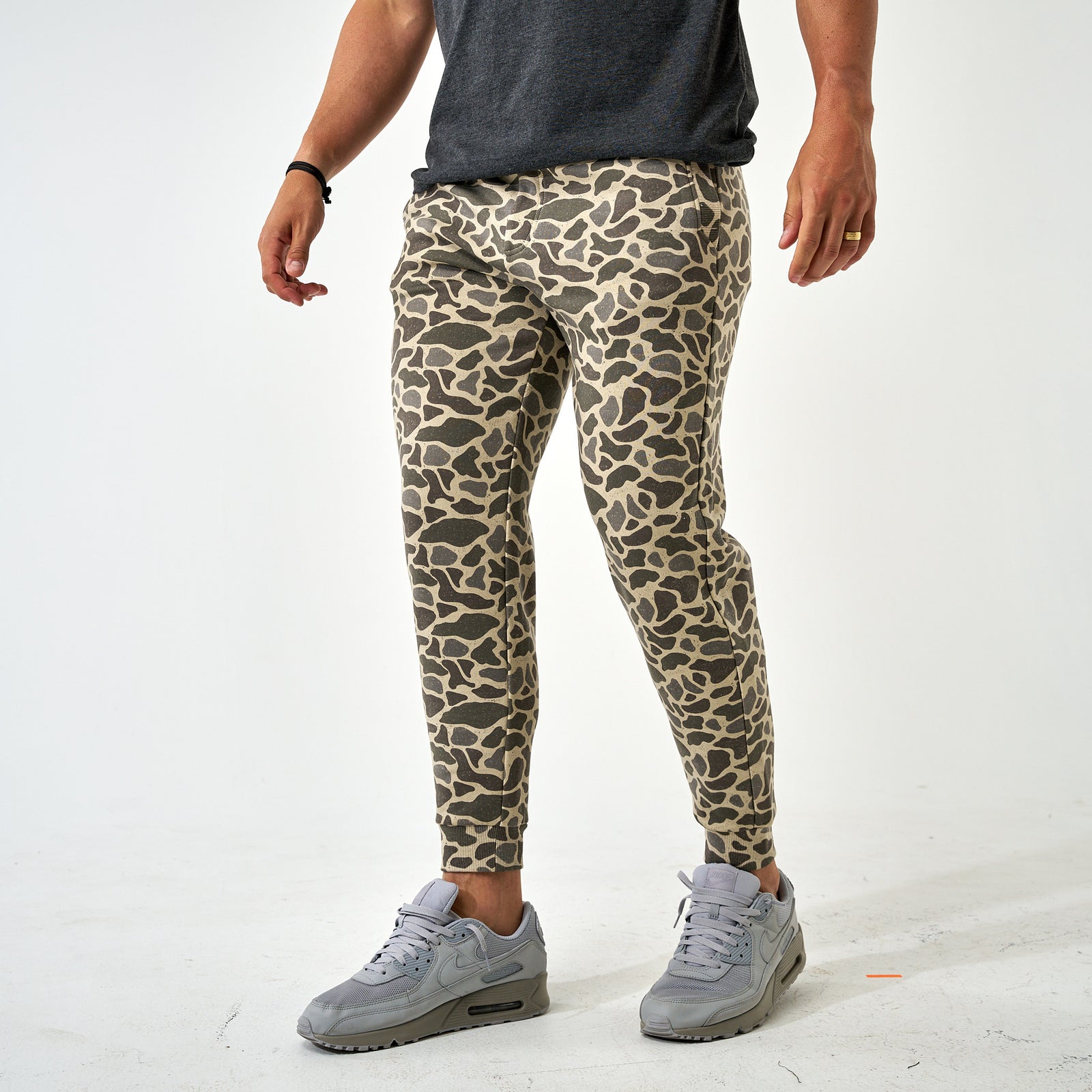 Front angle view of men’s joggers in camo print, styled with a dark tee and gray sneakers.
