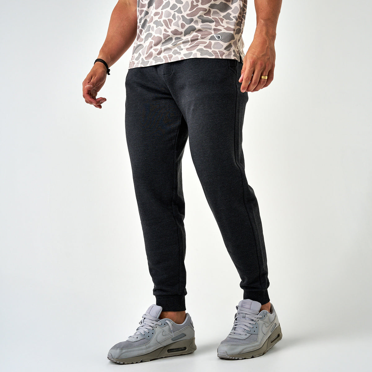Front angled view of men’s dark charcoal joggers featuring tapered legs, ribbed cuffs, and side pockets, styled with gray sneakers.