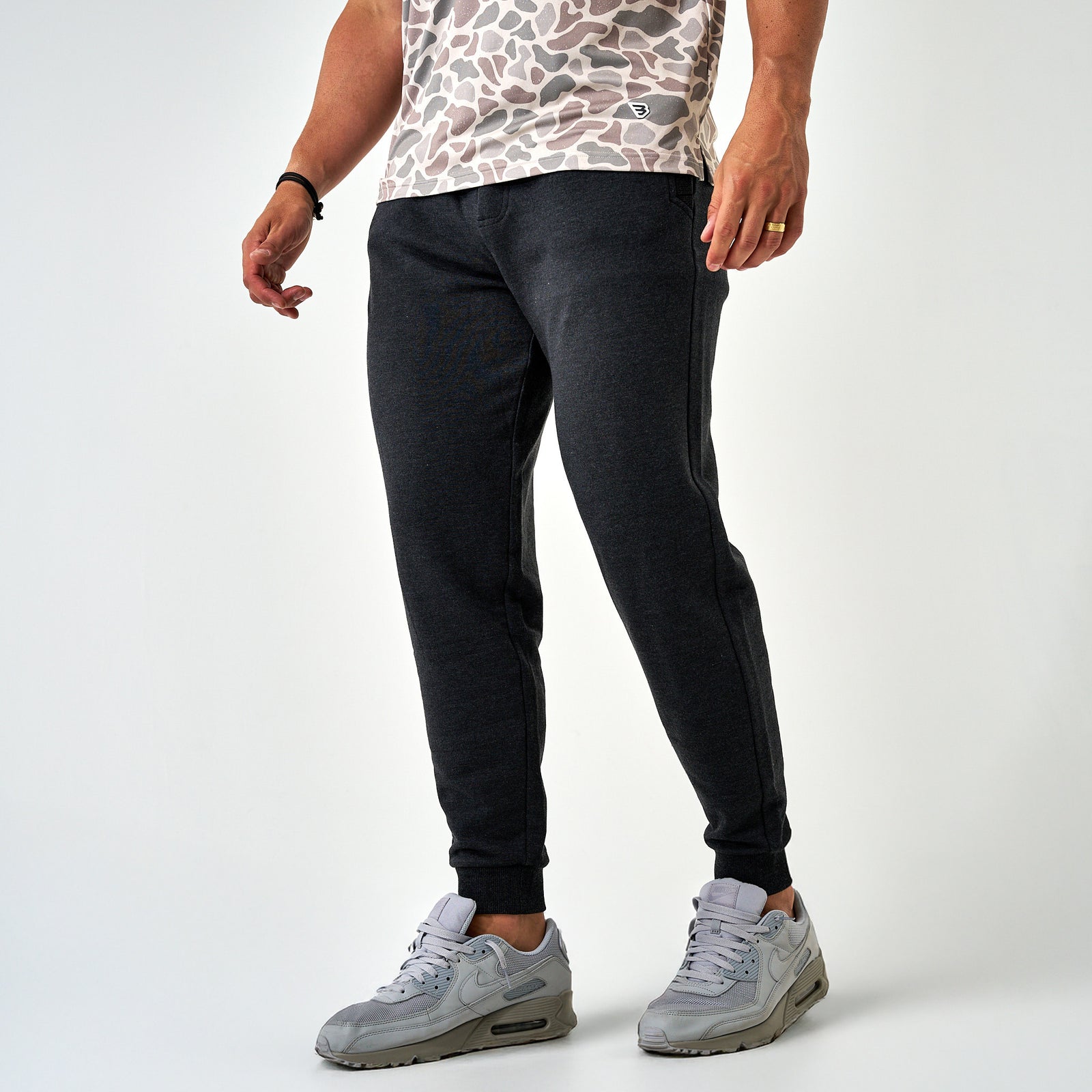Front angled view of men’s dark charcoal joggers featuring tapered legs, ribbed cuffs, and side pockets, styled with gray sneakers.