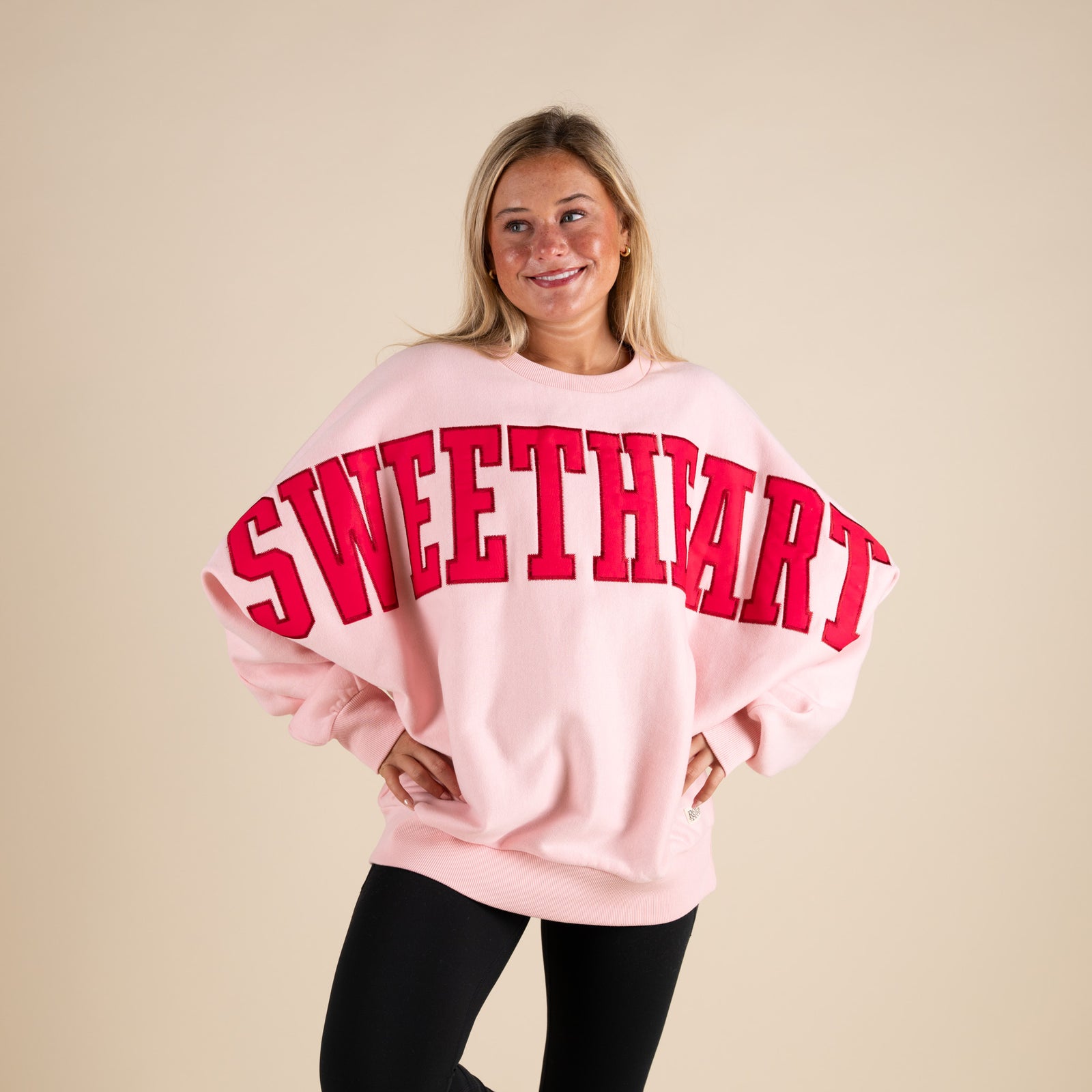 Person wearing a pink sweatshirt with 'SWEETHART' in red text on a beige background