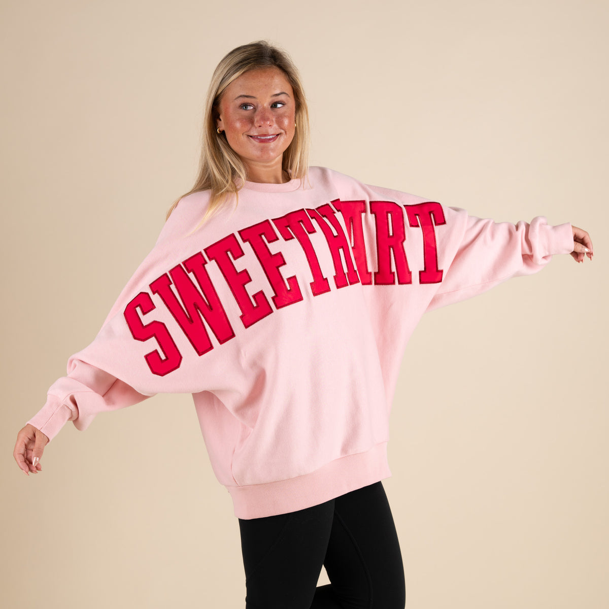 Person wearing a pink sweatshirt with 'SWEETHEART' in red text on a beige background