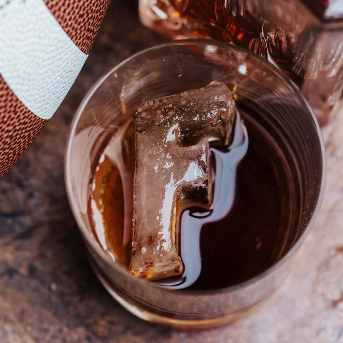 Drink glass on table with F-shaped ice cube floating in dark beverage