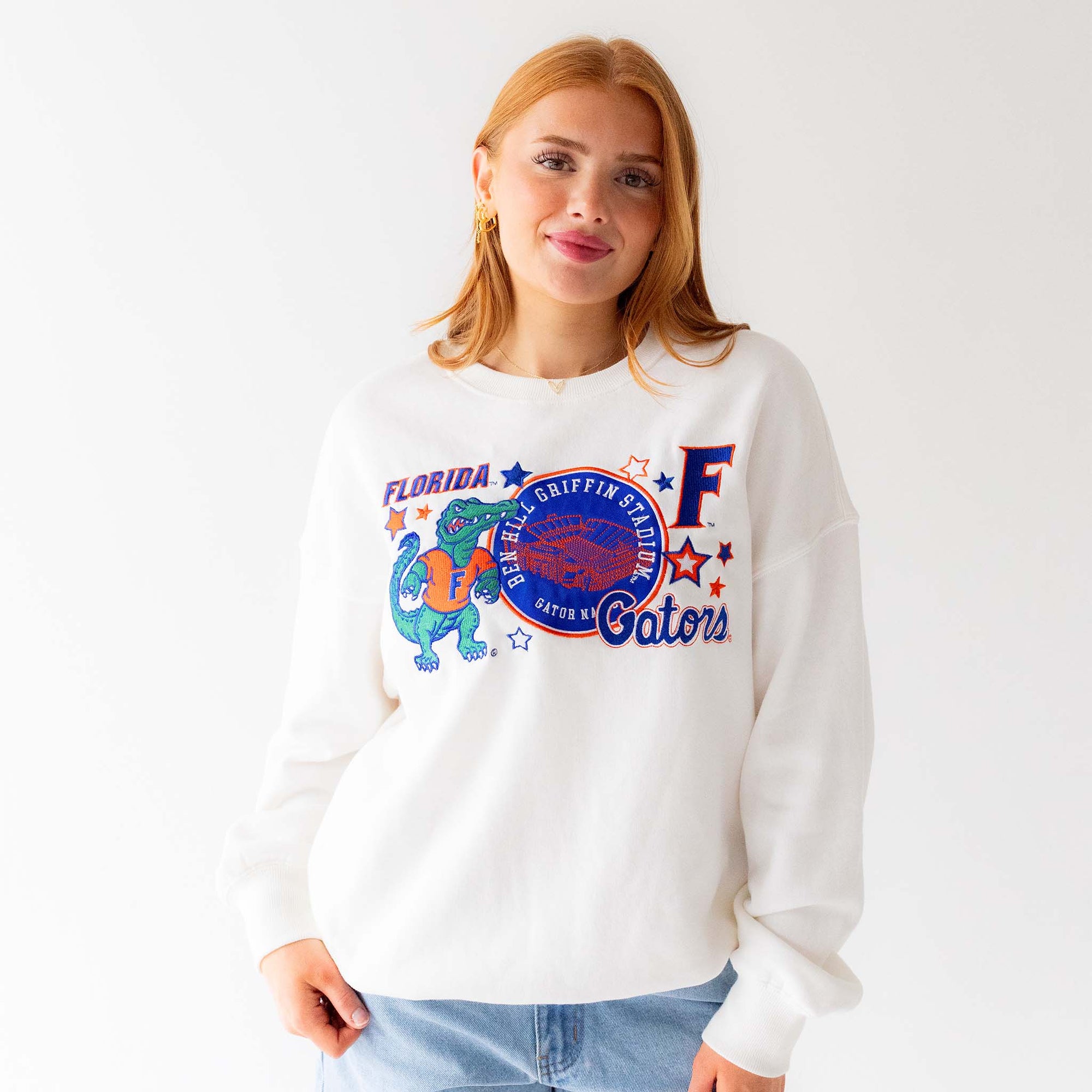 Woman wearing a white crewneck sweatshirt with embroidered Florida Gators graphics including Albert the Alligator mascot, Ben Hill Griffin Stadium patch, letter “F,” and stars.