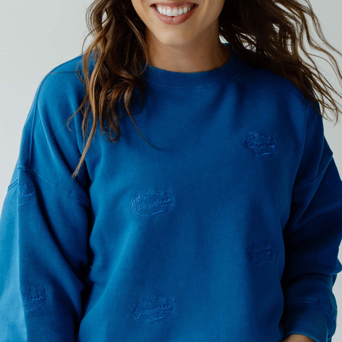 Close-up of royal blue crewneck sweatshirt showing tonal embroidered Florida Gators head logo pattern.