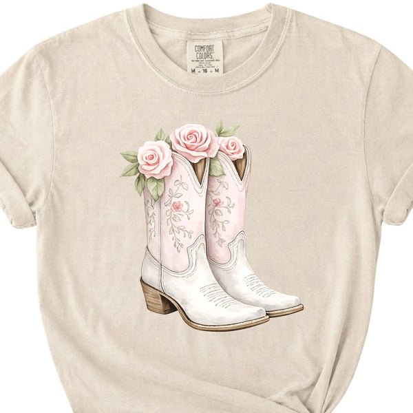 Close-up of ivory t-shirt graphic showing pink floral cowboy boots with roses and delicate western-style details.
