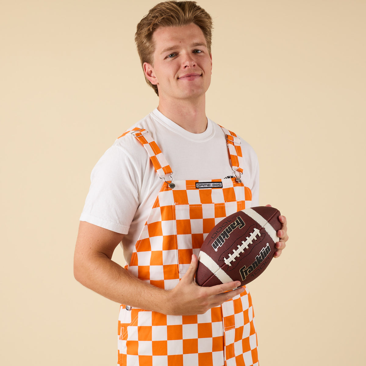 Man posing for a product photo in Orange and white checkered overalls.