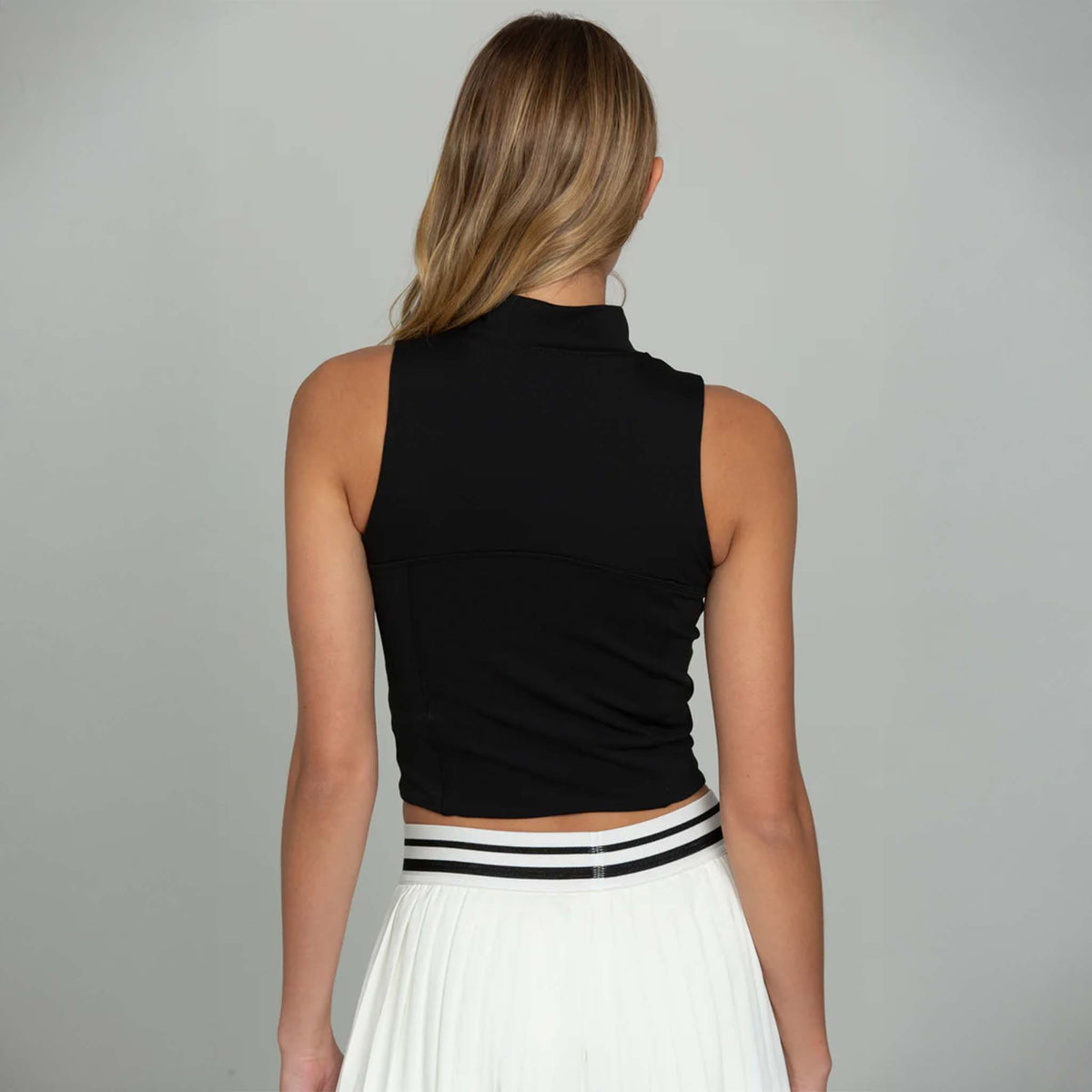 Back view of black cropped tank with mock neck and zip front paired with white skirt.