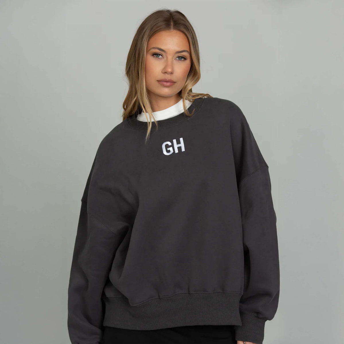 Woman modeling a black gold hinge crewneck sweatshirt with white GH logo embroidered on the front middle chest.