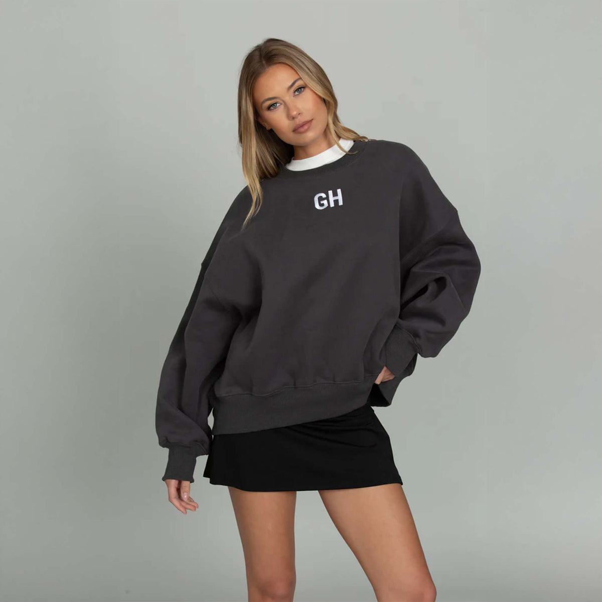 Woman modeling a black gold hinge crewneck sweatshirt with white GH logo embroidered on the front middle chest.