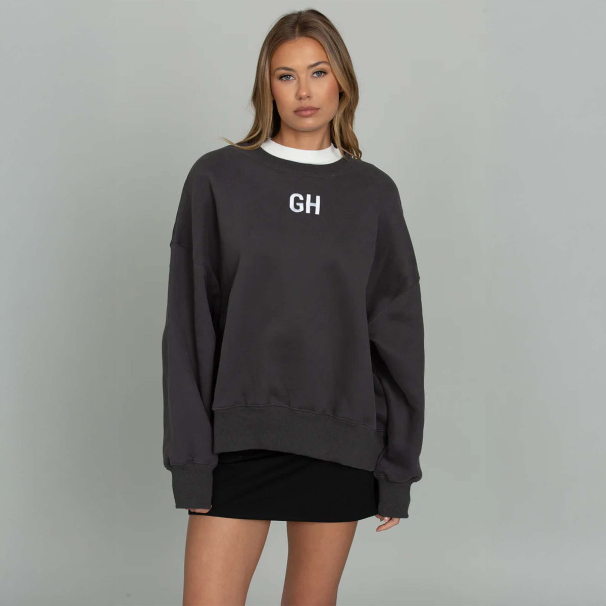 Woman modeling a black gold hinge crewneck sweatshirt with white GH logo embroidered on the front middle chest.