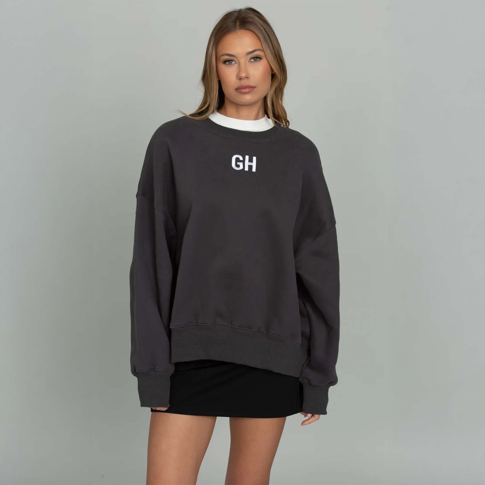 Woman modeling a black gold hinge crewneck sweatshirt with white GH logo embroidered on the front middle chest.