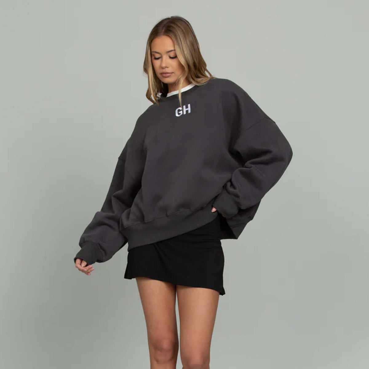 Woman modeling a black gold hinge crewneck sweatshirt with white GH logo embroidered on the front middle chest.