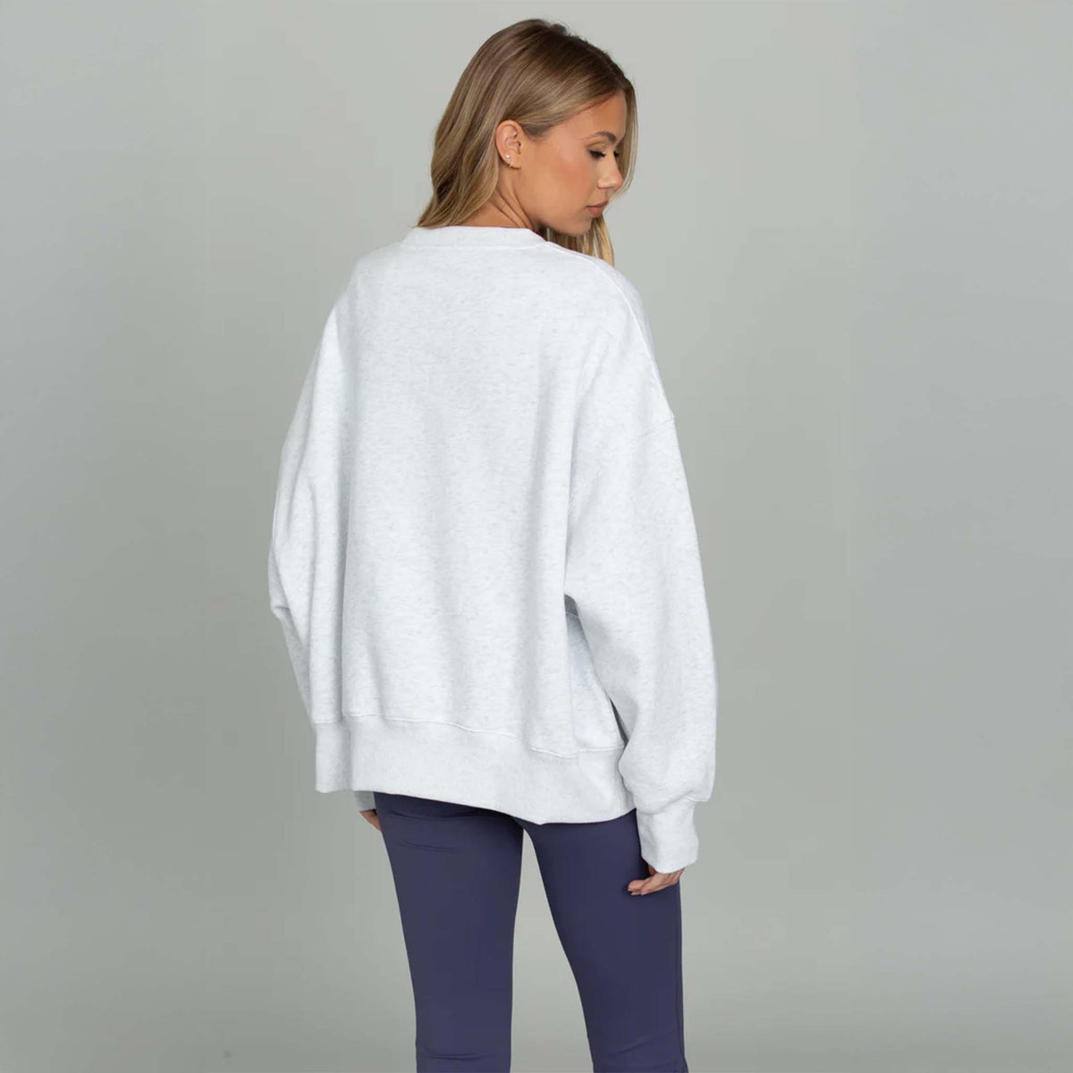 Woman wearing a white sweater and purple pants on a gray background