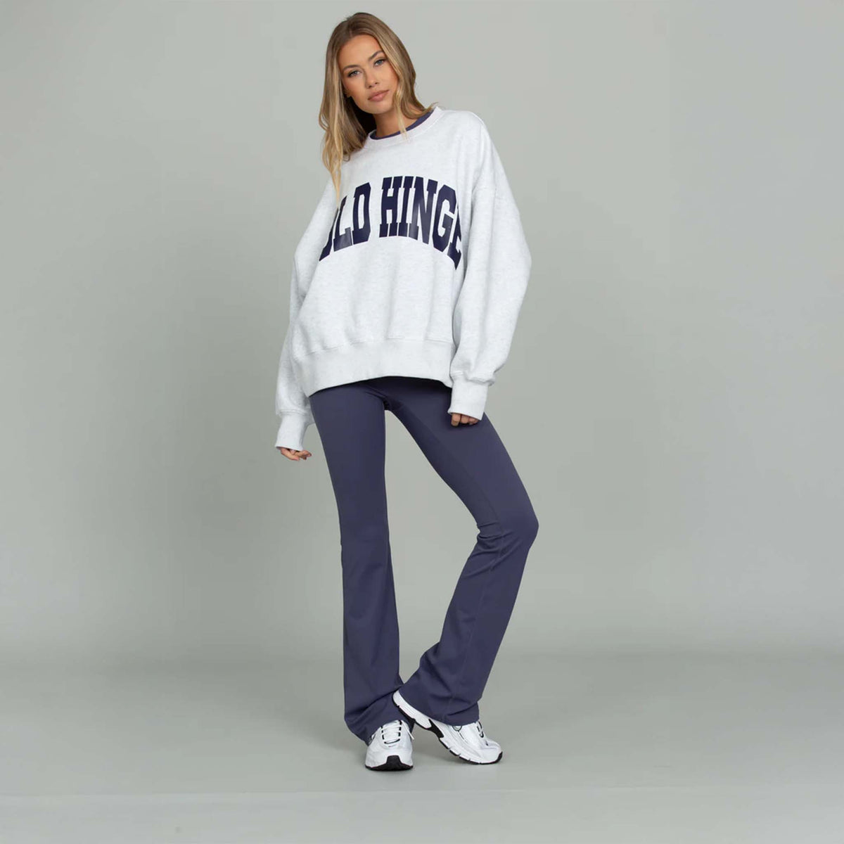 Woman wearing a white sweatshirt with text and dark pants on a gray background