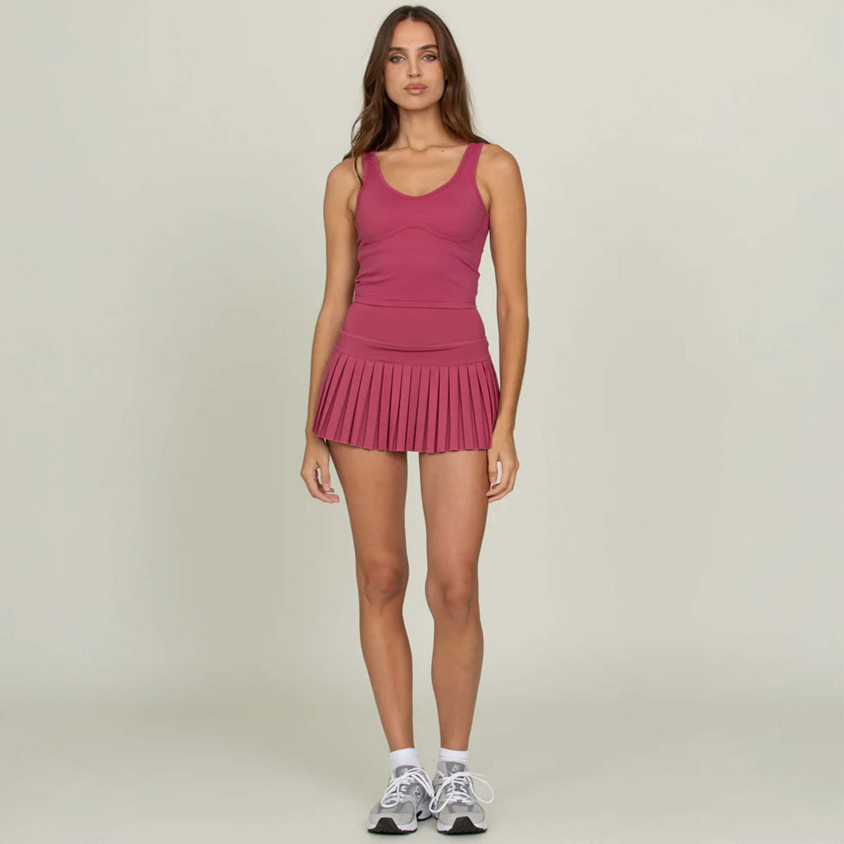 Woman wearing Gold Hinge cropped tank in raspberry with pleated tennis skirt, front view.
