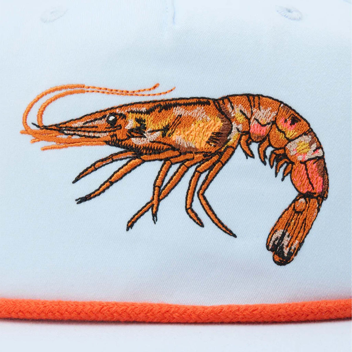 Close-up of embroidered orange shrimp design on front of Duck Camp Icewater blue cap with orange rope trim.