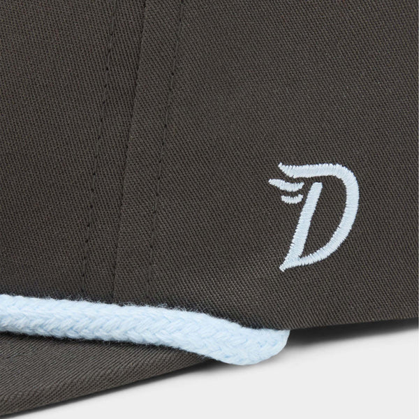 Side detail of Duck Camp Flying Pintail Hat in Raven with embroidered white “D” wing logo above light blue rope trim on brim.