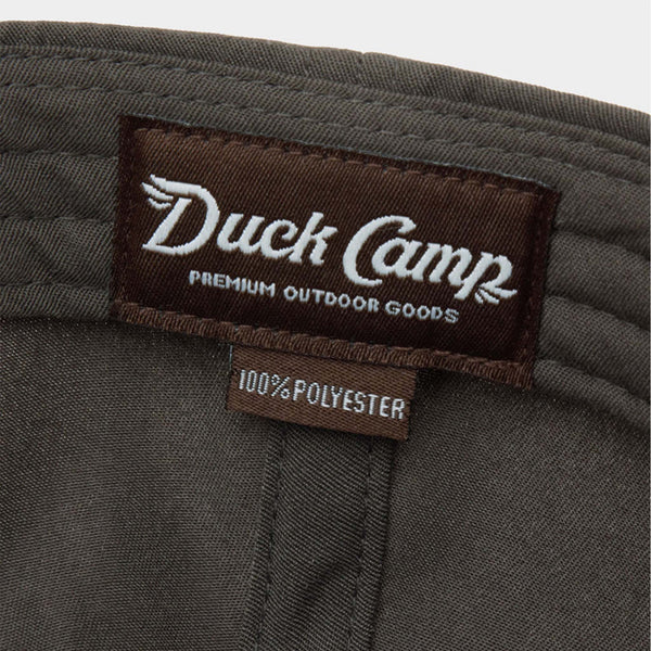 Inside view of Duck Camp Flying Pintail Hat in Raven showing brown “Duck Camp Premium Outdoor Goods” woven label with 100% polyester tag.