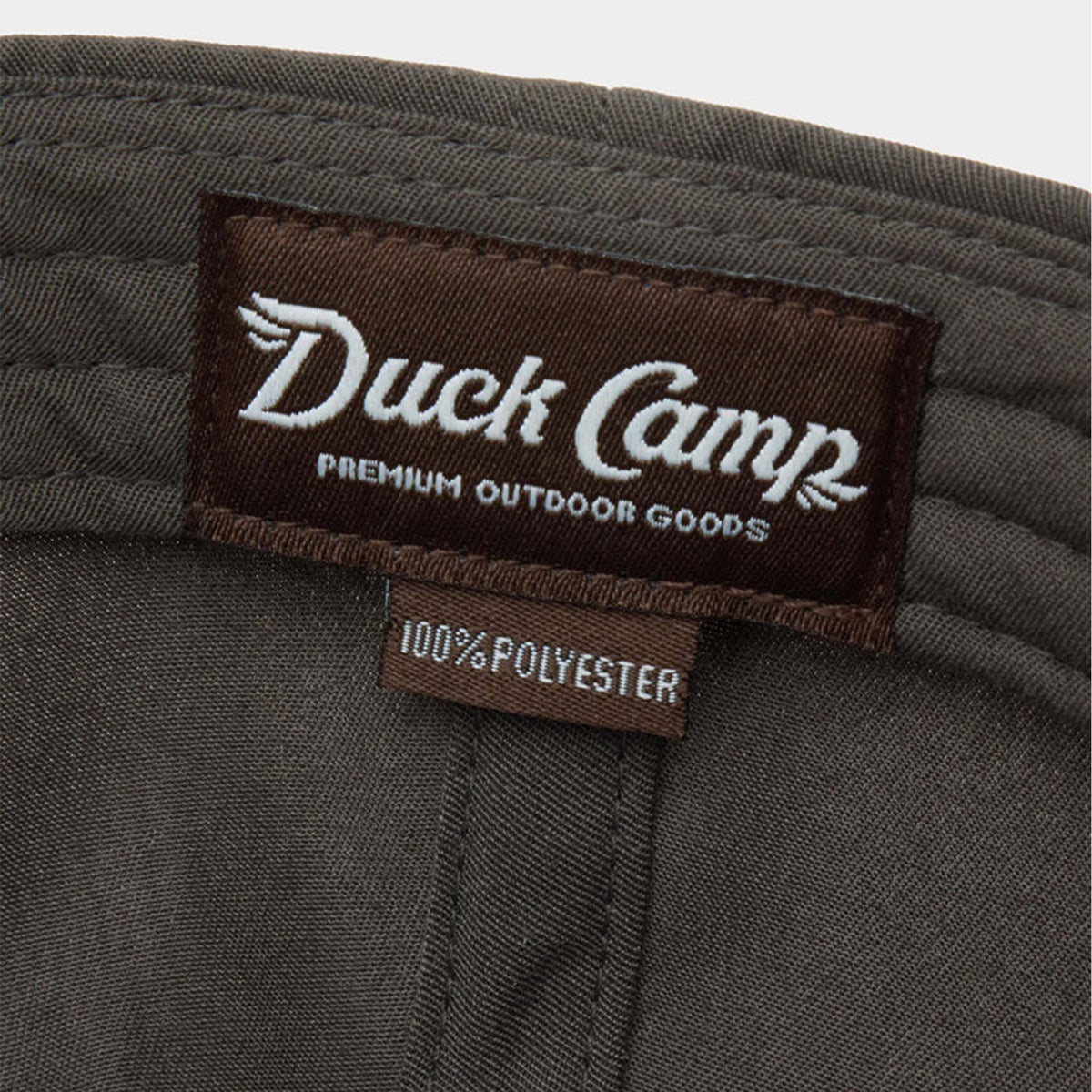 Inside view of Duck Camp Flying Pintail Hat in Raven showing brown “Duck Camp Premium Outdoor Goods” woven label with 100% polyester tag.