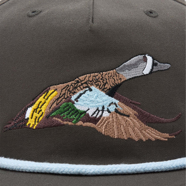 Close-up of Duck Camp Flying Pintail Hat in Raven with embroidered pintail duck in flight across the front panel, featuring brown, gray, green, yellow, and blue details.