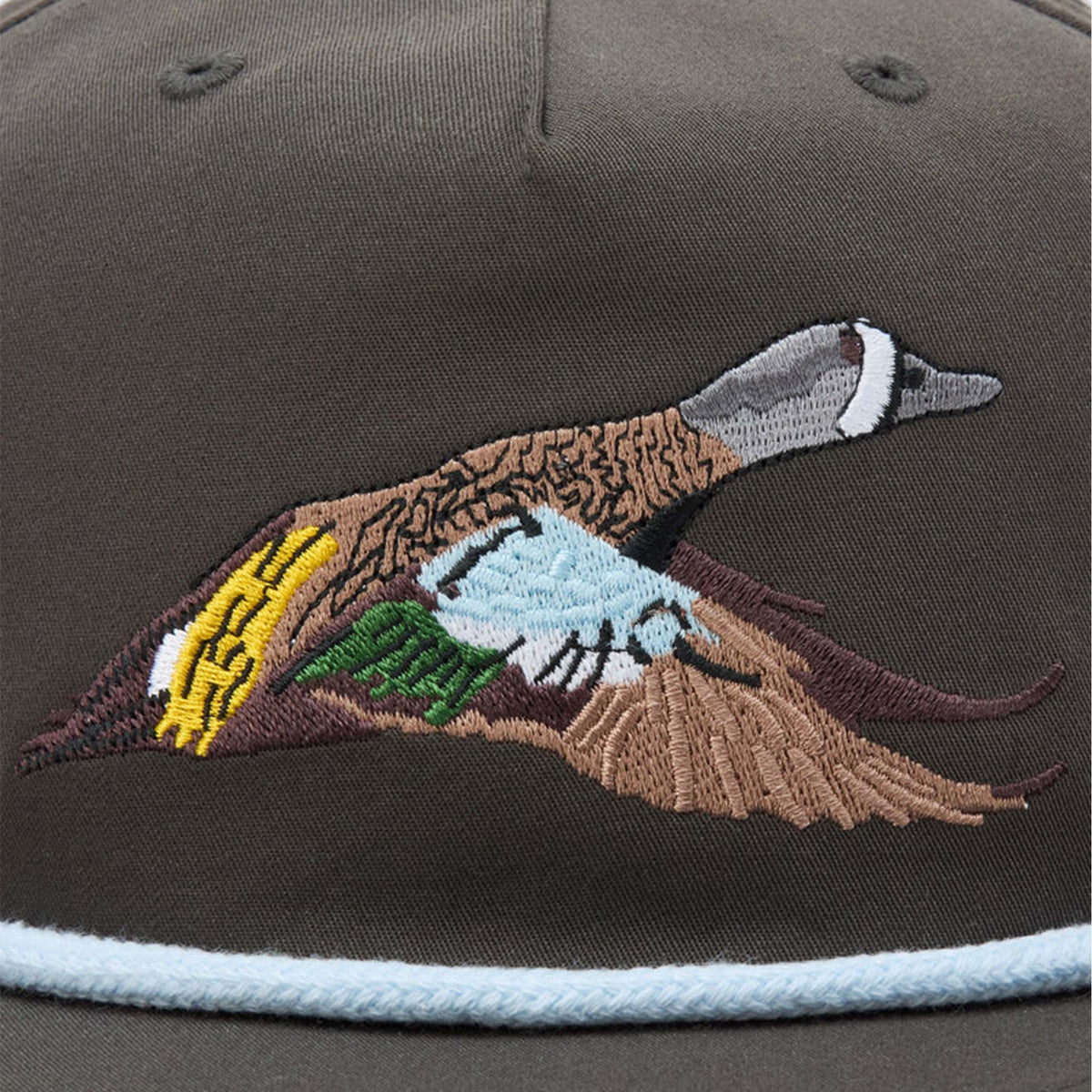 Close-up of Duck Camp Flying Pintail Hat in Raven with embroidered pintail duck in flight across the front panel, featuring brown, gray, green, yellow, and blue details.