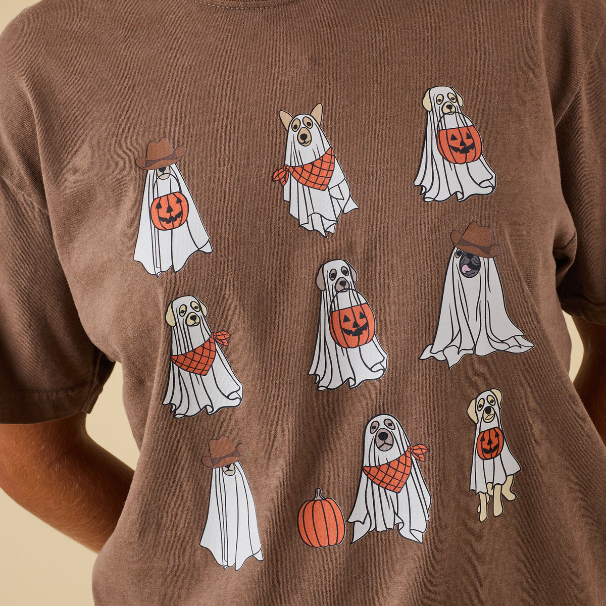 Close-up of ghost puppies Halloween design on brown t-shirt, including pumpkins, bandanas, and cowboy hats.