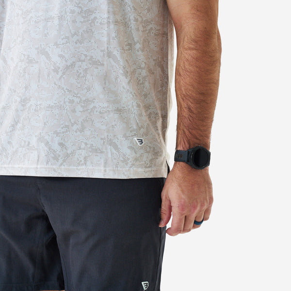 Close-up of a man wearing a light gray patterned short sleeve performance t-shirt and black shorts, showing subtle geometric print and small logo detail near the hem.