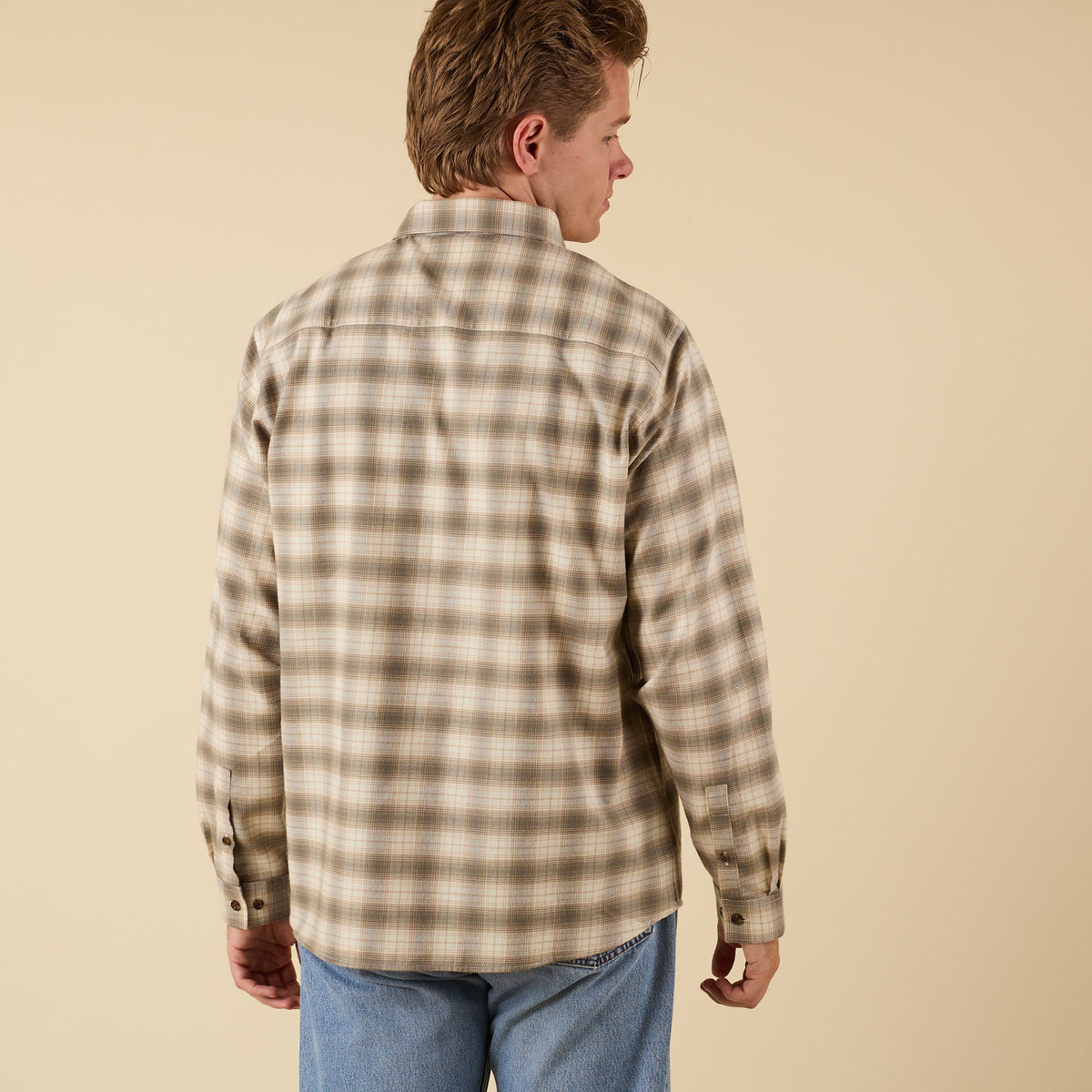 Man wearing a plaid shirt and jeans on a beige background