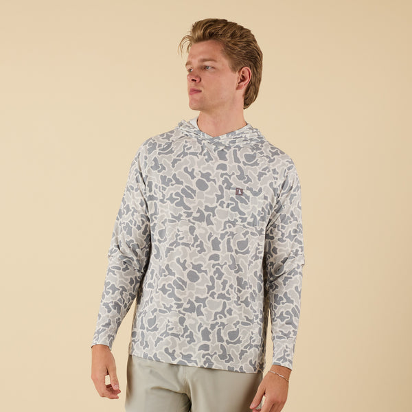 Man wearing a white camo long sleeve hooded t-shirt on a beige background.