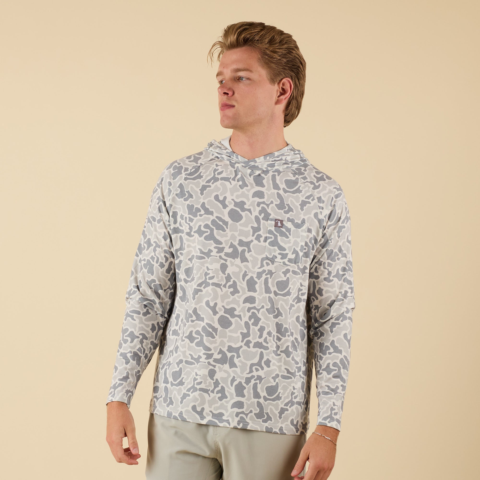 Man wearing a white camo long sleeve hooded t-shirt on a beige background.