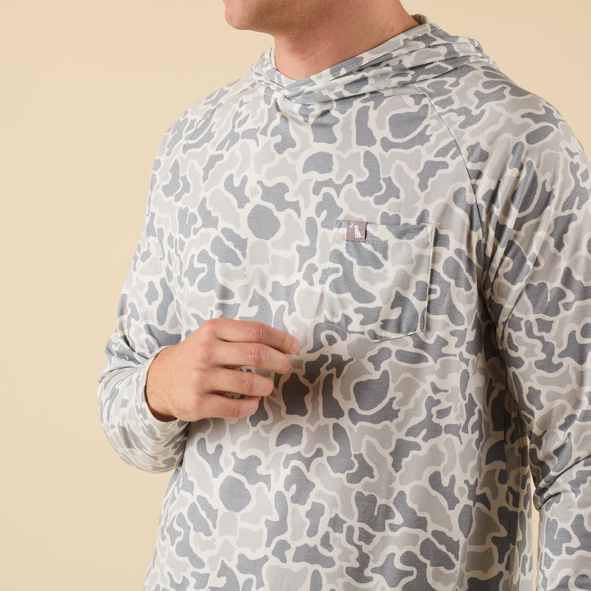 Man wearing a white camo long sleeve hooded t-shirt on a beige background.