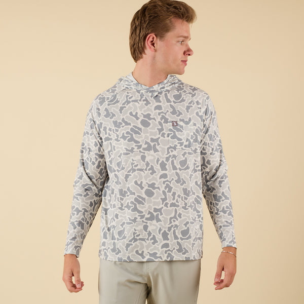 Man wearing a white camo long sleeve hooded t-shirt on a beige background.
