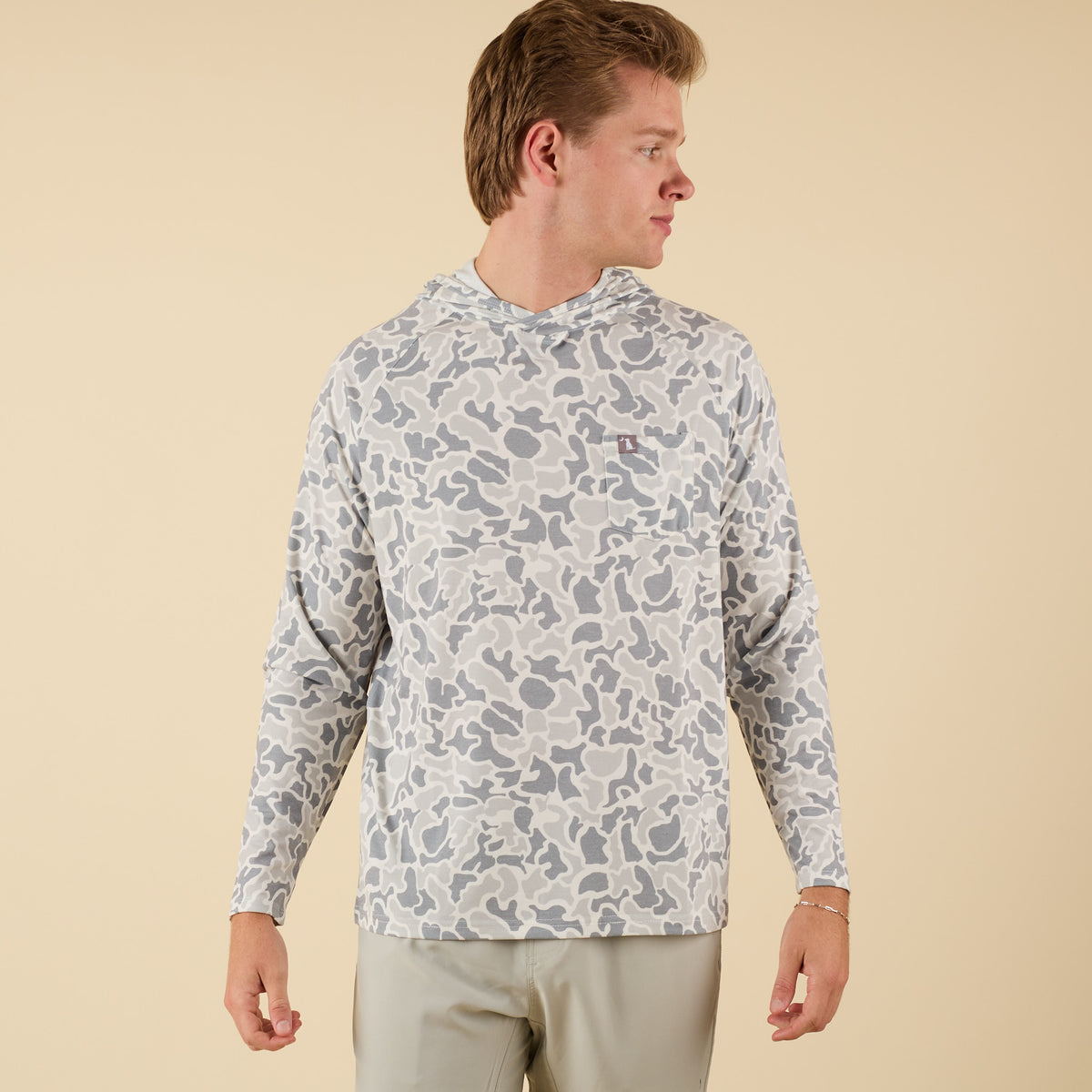 Man wearing a white camo long sleeve hooded t-shirt on a beige background.